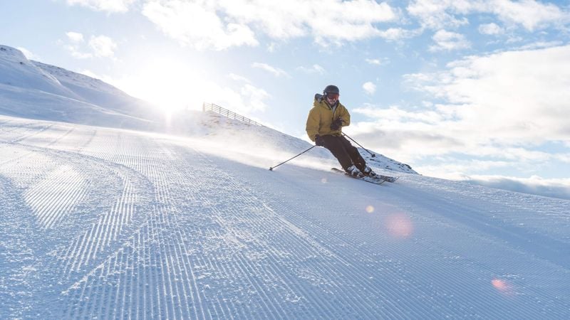 Person skiing down freshly groomed slope at sun rise.