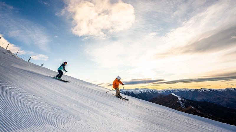 Two people skiing down a freshly groomed slope as the sun rises.