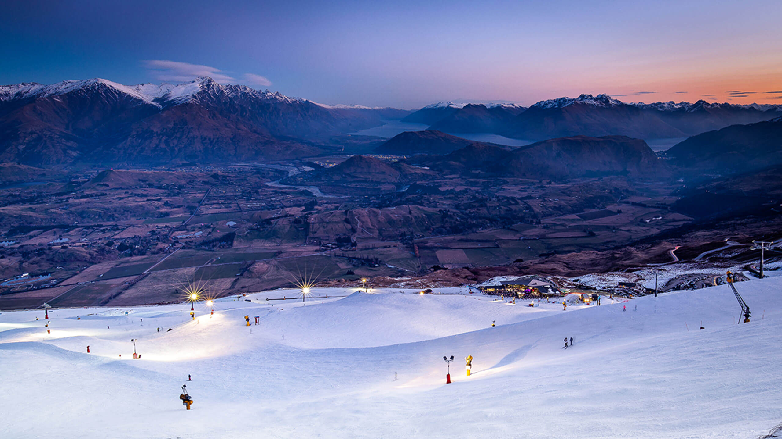 Snow covered slope with view of the mountains as the sun sets.