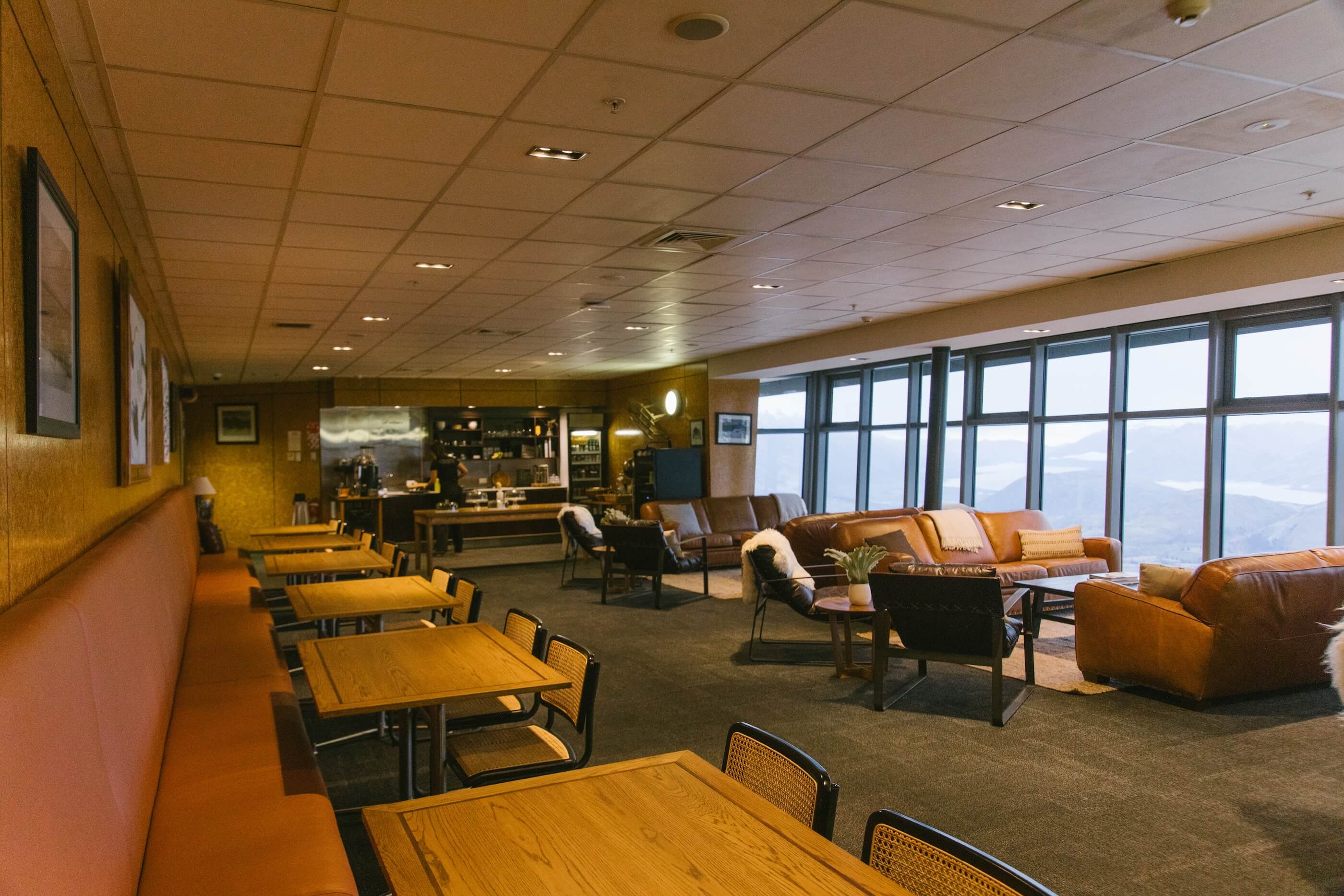 Spacious lounge with wooden tables, brown leather sofas, and large windows showing a mountain view.