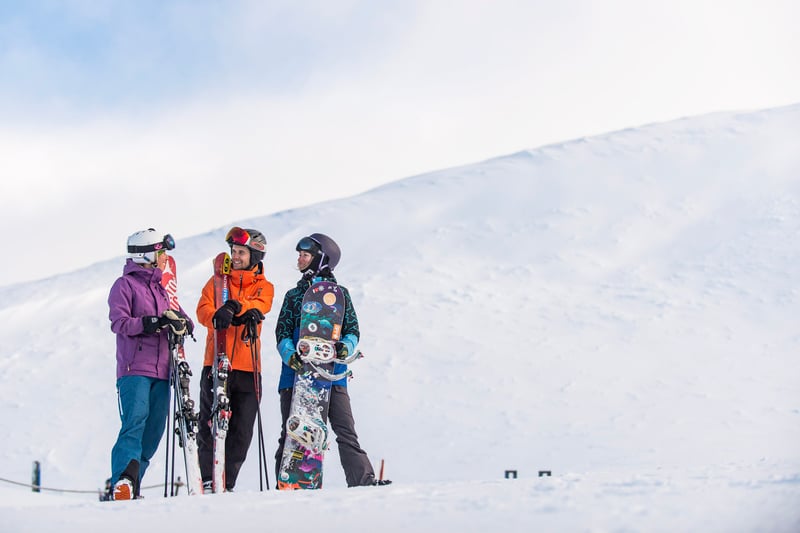 People standing in the snow holding their skis and snowboards.