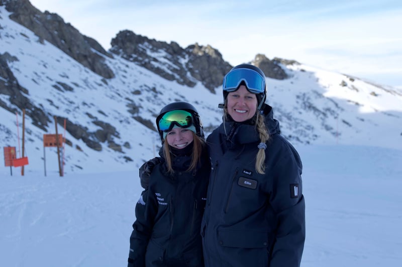 Two snowsports instructors smiling on a snow-covered mountain.
